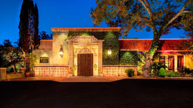 A mansion lit by residential outdoor lighting against the dull background of the evening sky