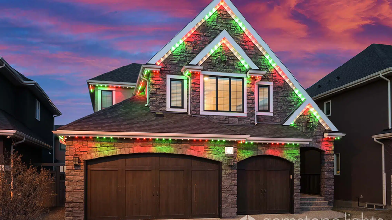 Two-story house with stone façade, adorned with holiday lights along the roofline