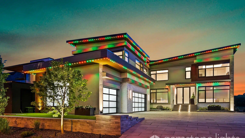 Contemporary house illuminated by permanent red, green, and yellow holiday lights along the roofline