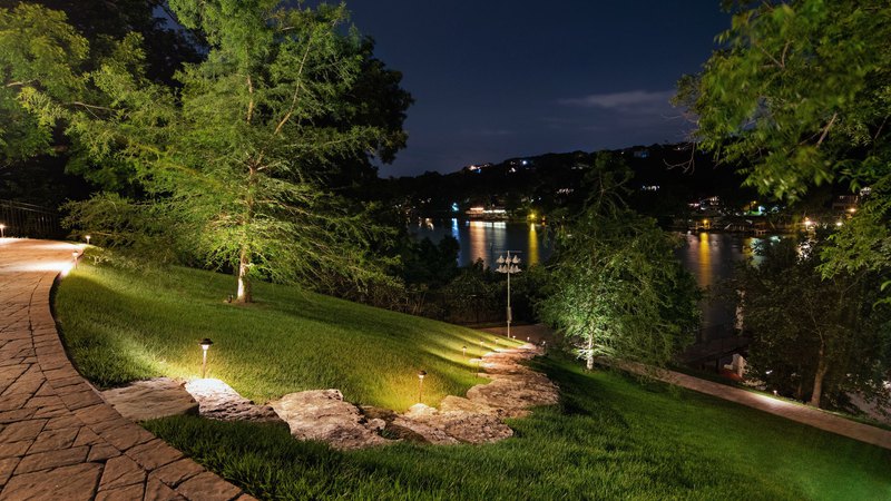 A lush green garden, lit by pathway lighting, showing a walkway cutting through the grass