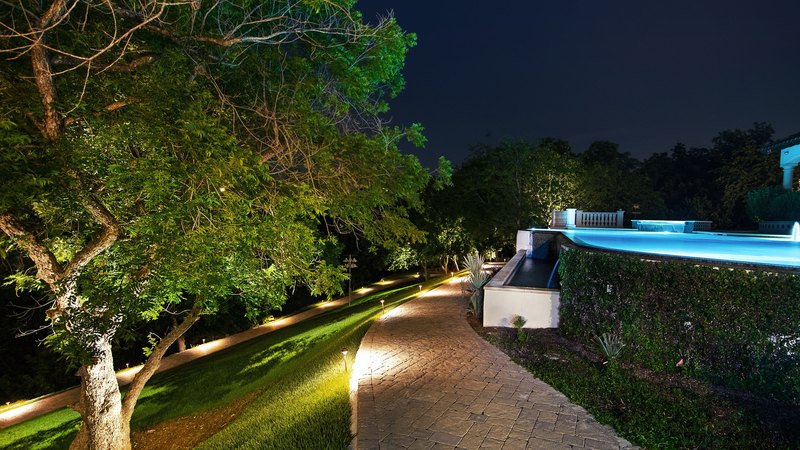 A walkway cutting through the grass, bordering a swimming pool gleaming under led pathway lights